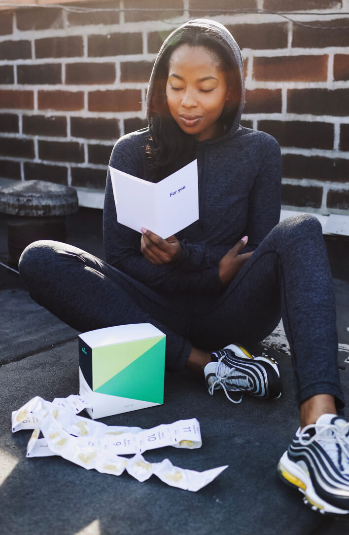 A woman sitting on the ground outside reading her Baze Personalized Supplement Fact Cards with her supplement daily packs scattered on the ground at her feet 